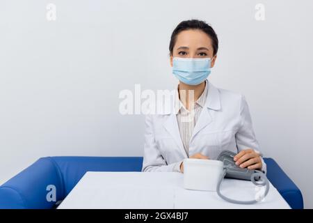 dottore in camice bianco e tonometro di tenuta maschera medica Foto Stock