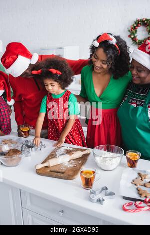 felice famiglia afroamericana a babbo natale cappelli vicino ragazza preparare biscotti di natale Foto Stock