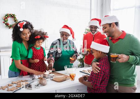 happy famiglia afroamericana bevendo tè alla cannella arancione mentre si preparano biscotti di natale in cucina Foto Stock