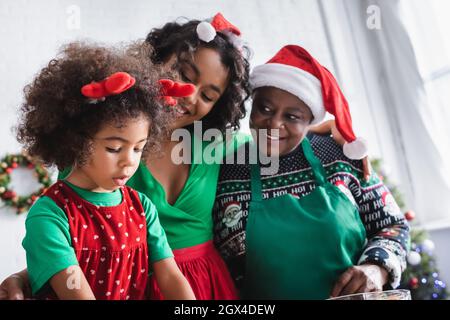 le donne afro-americane compiacenti in cappelli di santa guardando la ragazza in corna di renna fascia Foto Stock