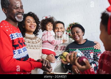 gioiosa famiglia afroamericana che guarda il ragazzo sfocato che tiene le palle di natale Foto Stock