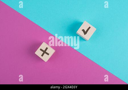 Cubi di legno con segno di spunta e croce su uno sfondo rosa e blu vibrante, minimalismo Foto Stock