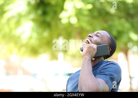 Un uomo nero felice ridendo a parlare con lo smartphone in un parco Foto Stock