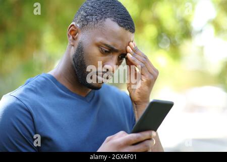 Uomo nero preoccupato che controlla i contenuti dello smartphone in un parco Foto Stock
