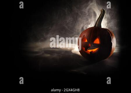 Halloween, zucca arancione con faccia luminosa su sfondo nero. Esce fumo denso. Foto Stock