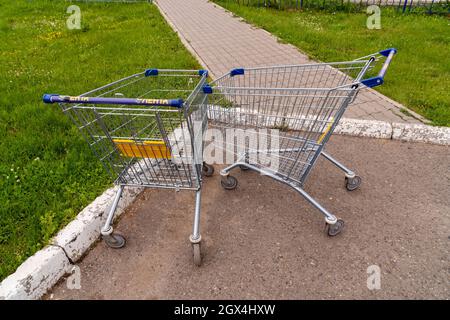 Due carrelli vuoti per la drogheria con il logo e il nome dell'ipermercato - la Lenta - in russo, si trovano abbandonati sul marciapiede in estate. Foto Stock