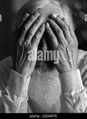 Un anziano stanco, rotto, rassegnato, preoccupato si siede davanti ad un computer portatile e gli copre il volto con la mano. Foto Stock