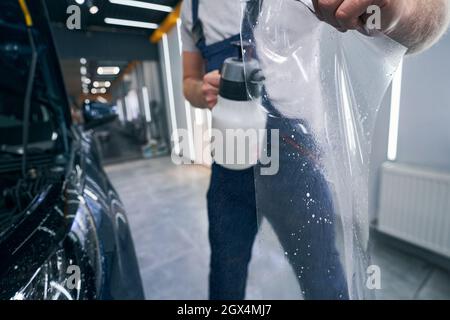 Detailer lavoratore wets da spray PPF closeup. Si applica la pellicola protettiva per auto Foto Stock