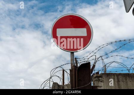 Nessun cartello stradale d'ingresso si trova su una recinzione in cemento con filo spinato sullo sfondo di un bel cielo. Foto Stock