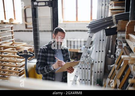 Carpentiere maschio maturo che fa l'inventario all'interno in officina di carpenteria. Concetto di piccola impresa. Foto Stock