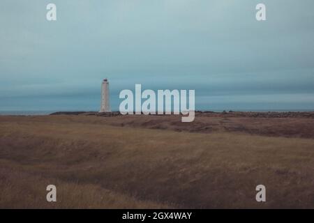 Vista panoramica del faro di Malarrif a est dell'islanda in una giornata nuvolosa. Alto faro in islanda di colore grigio e nuvole spesse sopra. Foto Stock