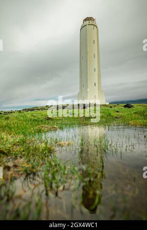 Vista panoramica del faro di Malarrif a est dell'islanda in una giornata nuvolosa. Faro alto in islanda di colore grigio e le nuvole spesse sopra e si rifla Foto Stock