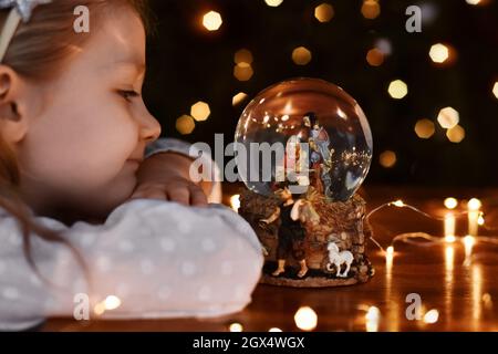 Ragazza che guarda una palla di vetro con una scena della nascita di Gesù Cristo Foto Stock