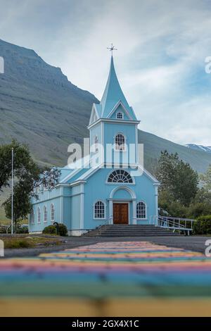 Bella piccola chiesa di legno nel villaggio di Seydisfjordur, Islanda, durante la sera con sentiero arcobaleno che conduce all'ingresso. Foto Stock