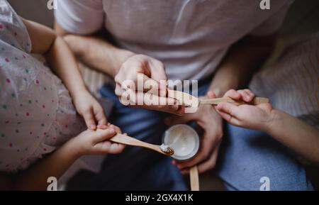 Vista dall'alto delle mani di padre irriconoscibile con due bambini piccoli che spazzolano i denti in casa, concetto di stile di vita sostenibile. Foto Stock