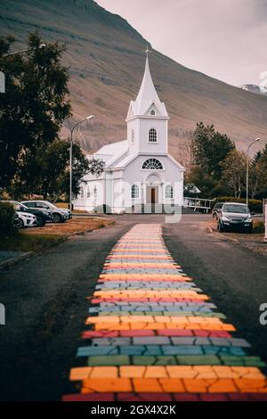 Bella piccola chiesa di legno nel villaggio di Seydisfjordur, Islanda, durante la sera con sentiero arcobaleno che conduce all'ingresso. Foto Stock