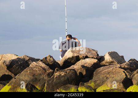 Primo piano di un uomo seduto su un molo di roccia che ha muschio verde al Sunken Meaow state Park pesca. Foto Stock