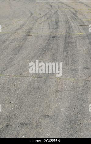 Asfalto grigio con cingoli pneumatici neri. Una vecchia strada di campagna con crepe. Cingoli delle ruote curvi in curva in autostrada. Foto Stock