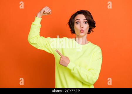 Foto di stupito giovane felice donna punto dito bicipite flex raccomandare isolato su sfondo arancione Foto Stock