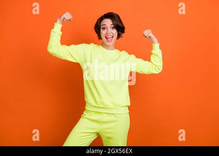 Foto di felice allegro giovane forte donna mostra mani muscoli buon umore isolato su sfondo di colore arancione Foto Stock