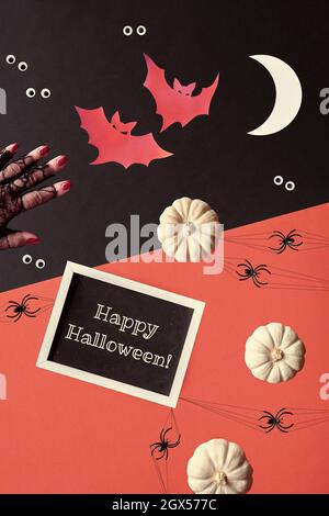 Composizione astratta di Halloween in rosso, nero e bianco. Texte sur Happy Halloween sulla lavagna. Sagome di carta di pipistrelli, mezzaluna luna. Occhi googly Foto Stock