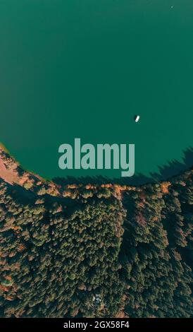 Vista aerea dall'alto verso il basso di una barca nella stagione autunnale sopra il lago vulcanico di Saint Anne (Sfanta Ana). Foresta e acqua. Harghita, Romania, in autunno Foto Stock