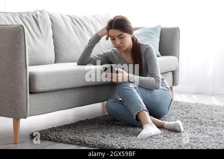 Sconvolto frustrato graziosa signora millenaria caucasica che soffre di depressione seduta sul pavimento e leggere il messaggio Foto Stock