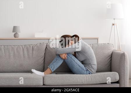 Infelice donna millenaria caucasica che soffre di depressione e solitudine, seduta sul divano a casa Foto Stock