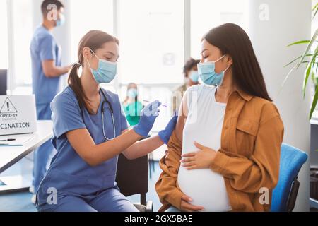 Donna incinta che riceve l'iniezione di vaccino in Arm in Health Center Foto Stock