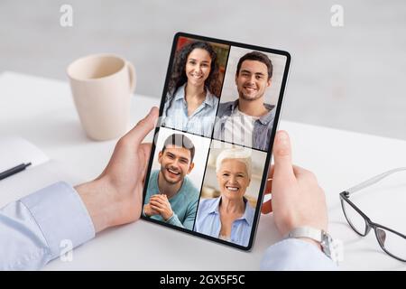 L'uomo d'affari caucasico, millenario e tagliato, utilizza il tablet per effettuare chiamate online con diversi giovani e adulti sullo schermo Foto Stock