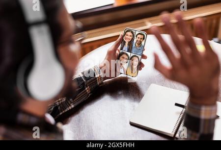 Giovane indiano irriconoscibile ha videochiamata con amici europei sorridenti, colpo di testa sullo schermo del telefono Foto Stock