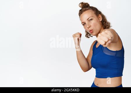 Lo sport swoman pratica pugni, indossa abbigliamento fitness e di lavoro, pugilato, mostrando mosse di combattimento, in piedi su sfondo bianco Foto Stock