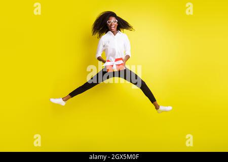 Intera lunghezza corpo dimensione foto donna salto in alto mantenere confezione regalo a festa sorridente isolato vivido colore sfondo giallo Foto Stock