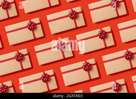 Modello senza giunture di scatole regalo di festa avvolte in carta artigianale con un arco rosso su sfondo rosso. Vista dall'alto. Foto Stock