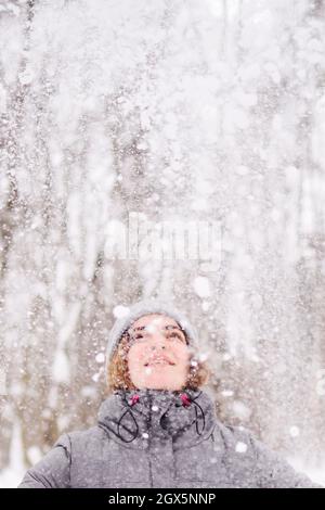 Una giovane donna guarda con gioia alla caduta della neve nella foresta. Foto Stock