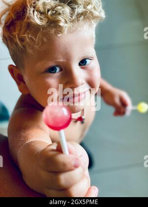 ragazzo biondo riccio che condivide una caramella su un bastone Foto Stock