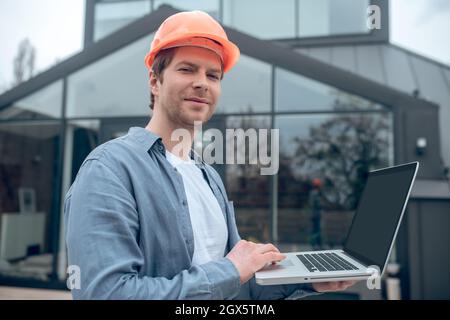 Uomo felice in casco di sicurezza che lavora su un computer portatile Foto Stock