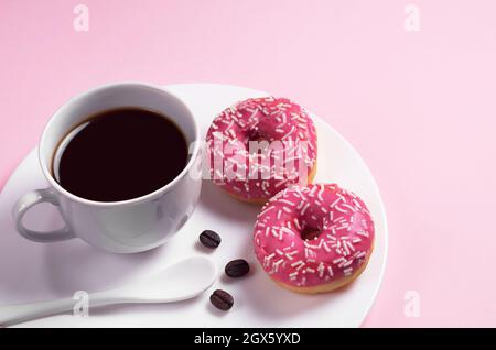 Ciambelle rosa con spruzzi e una tazza di caffè in piatto su sfondo colorato Foto Stock
