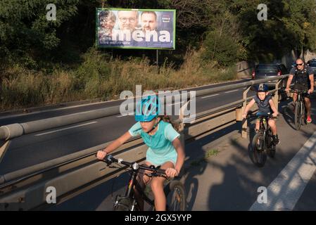 I ciclisti passano da un cartellone elettorale per la coalizione SPOLU posta sulla strada di Praga. Sul tabellone (da sinistra a destra) il leader della coalizione Marketa Pekarova Adamova del partito TOP09, Petr Fiala del partito ODS e Marian Jurecka del partito KDU-CSL. Le elezioni del Parlamento nella Repubblica ceca si terranno il 7 e 8 ottobre 2021. Foto Stock