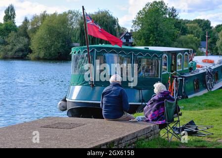 Una coppia anziana seduta sul lungofiume a Shepperton godendo un piccolo spuntino in un giorno d'estate Surrey Inghilterra Regno Unito Foto Stock