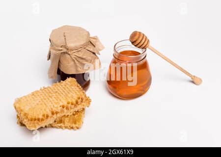 giare con miele giallo e marrone vicino al divaricatore di legno e nido d'ape su bianco Foto Stock