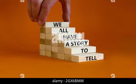 Abbiamo tutti una storia da raccontare Symbol. Blocchi di legno con parole 'abbiamo tutti una storia da raccontare'. Mano uomo d'affari. Bellissimo sfondo arancione. Azienda, p. Foto Stock