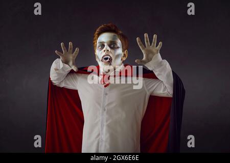 Studio ritratto di ragazzo che indossa il trucco spooky Halloween, finti fangs e vampiro mantello Foto Stock