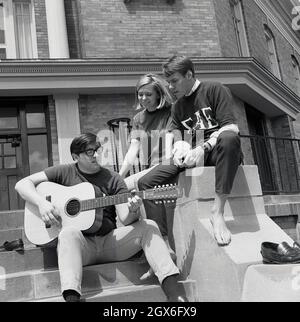 Anni '60, storico, tre studenti, uno con una chitarra acustica, gli altri due che lo ascoltano suonano all'esterno del campus della Bowling Green University, Ohio, USA. Il giovane suona una chitarra goya, un marchio usato all'epoca dal co strumenti musicali Hershman di New York, che li importava dalla società Levin in Svezia, rimproverandoli 'Goya', dopo l'artista spanista Francisco Goya, noto per aver presentato chitarre nei suoi dipinti. In quest'epoca, gli americani si sono presi un simpatia per la chitarra Goya d'epoca, che si è rivelata popolare soprattutto con i musicisti folkloristici. Foto Stock