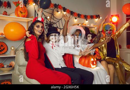 Amici felici in costumi spooky seduti tutti insieme sul divano al partito di Halloween Foto Stock