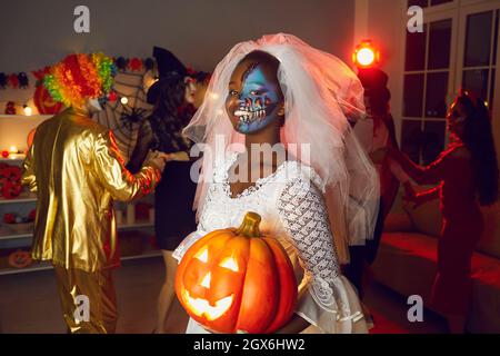 Ritratto di donna nera vestita come sposa morta che tiene jack-o-lanterna alla festa di Halloween Foto Stock