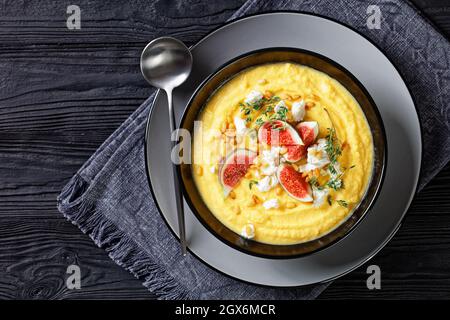 Zuppa di panna di zucca con timo servita su una ciotola nera con feta e fichi serviti su sfondo di legno con un cucchiaio, vista dall'alto, primo piano Foto Stock