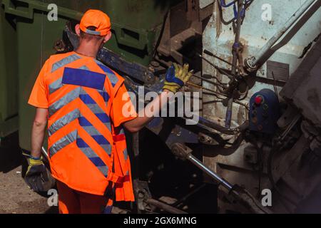 I lavoratori in uniformi di arancio chiaro stanno togliendo la spazzatura. Foto Stock