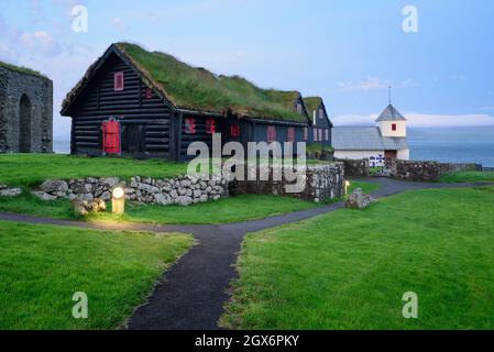 Antica casa colonica in tronchi di Kirkjuboargardur con tetto di erba sintetica e Chiesa di Olavskirkjan nel villaggio di Kirkjubour su Streymoy, Isole Faroe Foto Stock