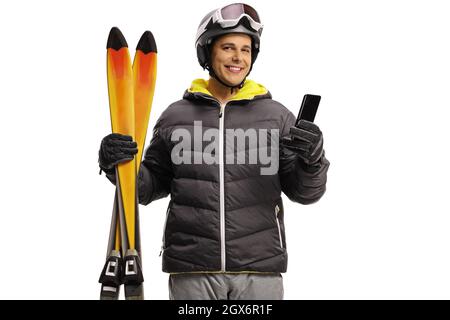 Giovane uomo con skiis sorridente e tenendo un cellulare isolato su uno sfondo bianco Foto Stock
